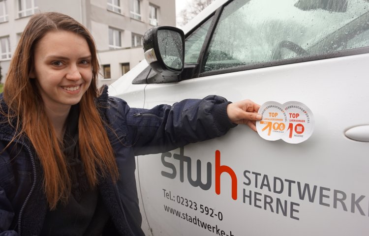 Melissa Olbrich, die eine Ausbildung zur Kfz-Mechatronikerin bei den Stadtwerken macht, klebt das neue Siegel auf eines der zahlreichen E-Autos des Unternehmens.